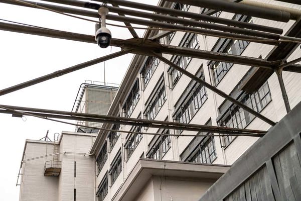 Stalen loopbrug met beveiligingscamera langs de witte gevel van een industrieel kantoorgebouw